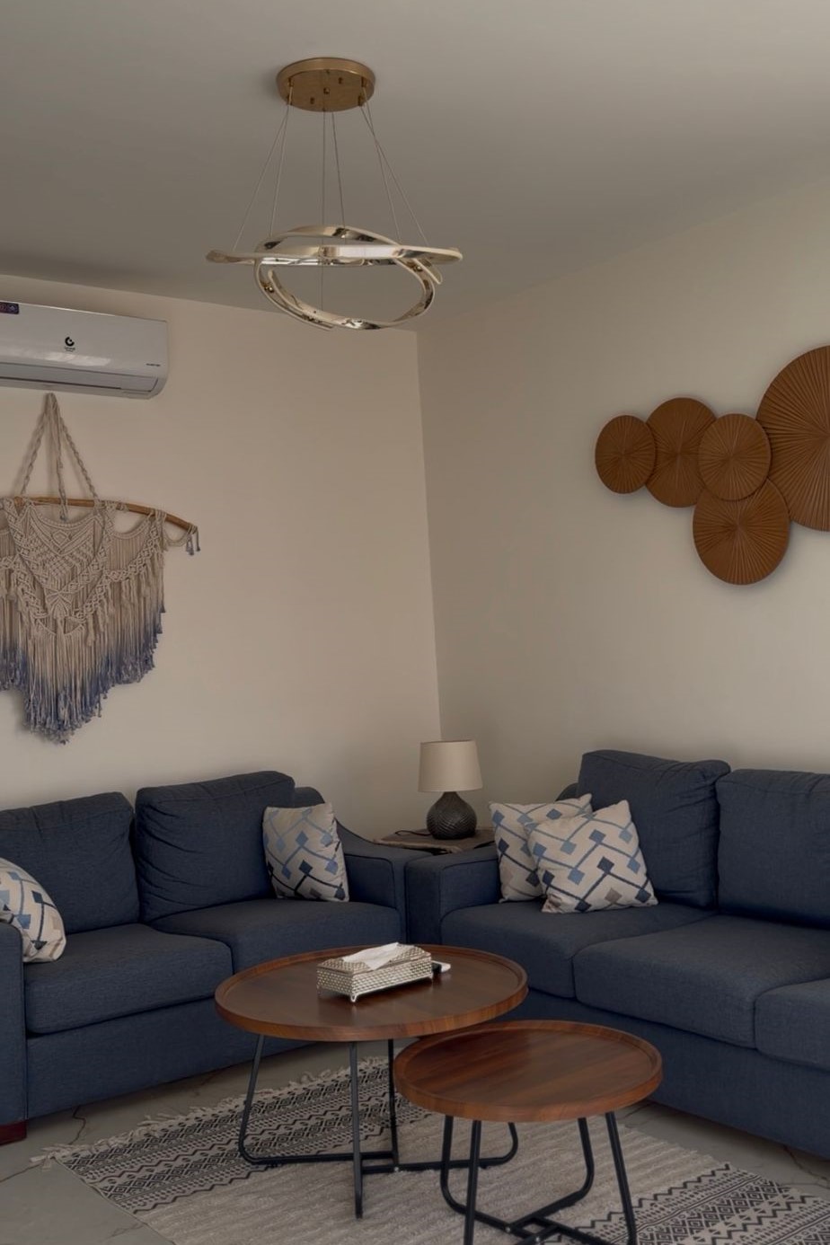 fa438b20-1502-40f7-bb0e-e787bbedb76e Cozy living room with a blue sectional sofa, patterned cushions, and two round wooden coffee tables on a light rug.