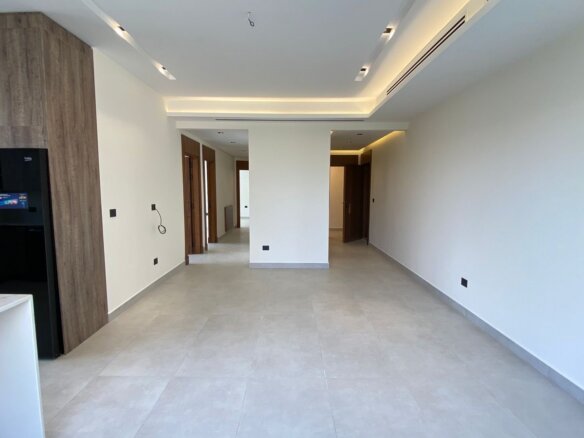 Modern open-plan kitchen and hallway with wood accent cabinetry, black fridge, and white island; bright, empty space awaiting decor.