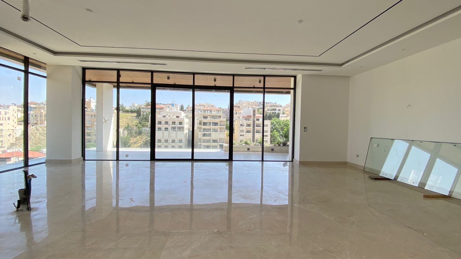 0151290e-bcbe-431c-93a5-95e7e7292752 Bright empty living room with polished marble floor and large glass doors to a balcony, overlooking a cityscape.