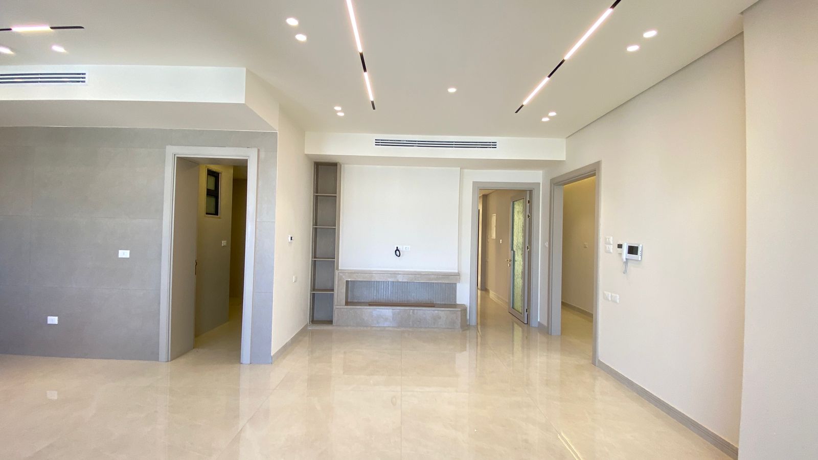 01e964bc-765a-447d-957c-0528c1ea3a2d Modern empty living room with glossy beige tile floor, recessed ceiling lights, and multiple doorways.