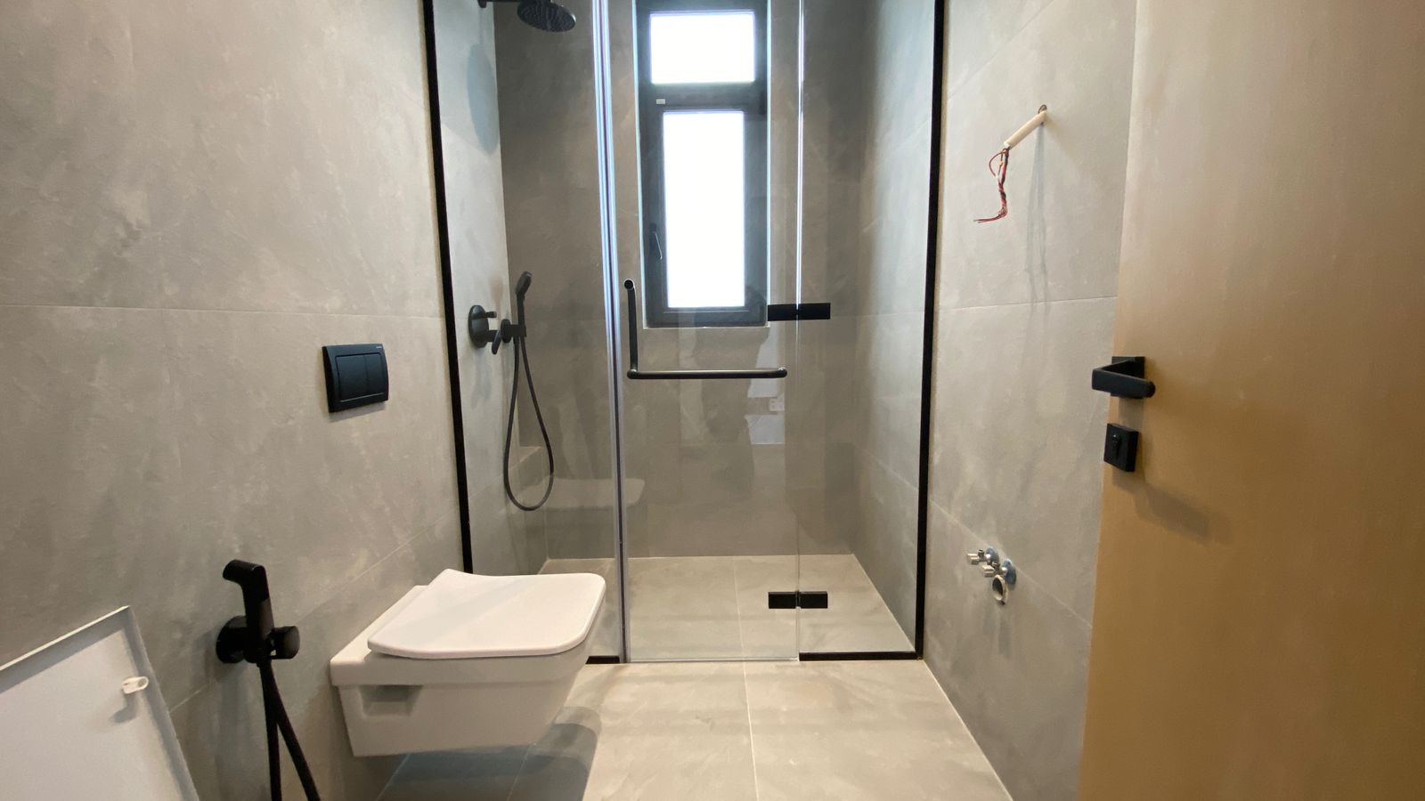 031ac17b-de03-426d-baa2-80320aca0419 Modern bathroom with a glass-walled walk-in shower, wall-hung toilet, and matte black fixtures on gray tiled walls.