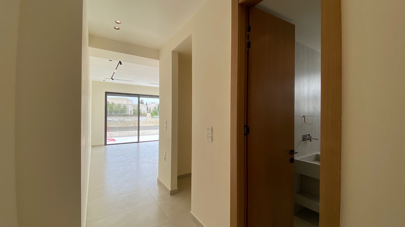 033698b1-6038-4409-8920-4780ede5b74d Bright empty hallway in a modern home, opening to a glass sliding door patio and a partially visible bathroom door on the right with a sink visible inside.