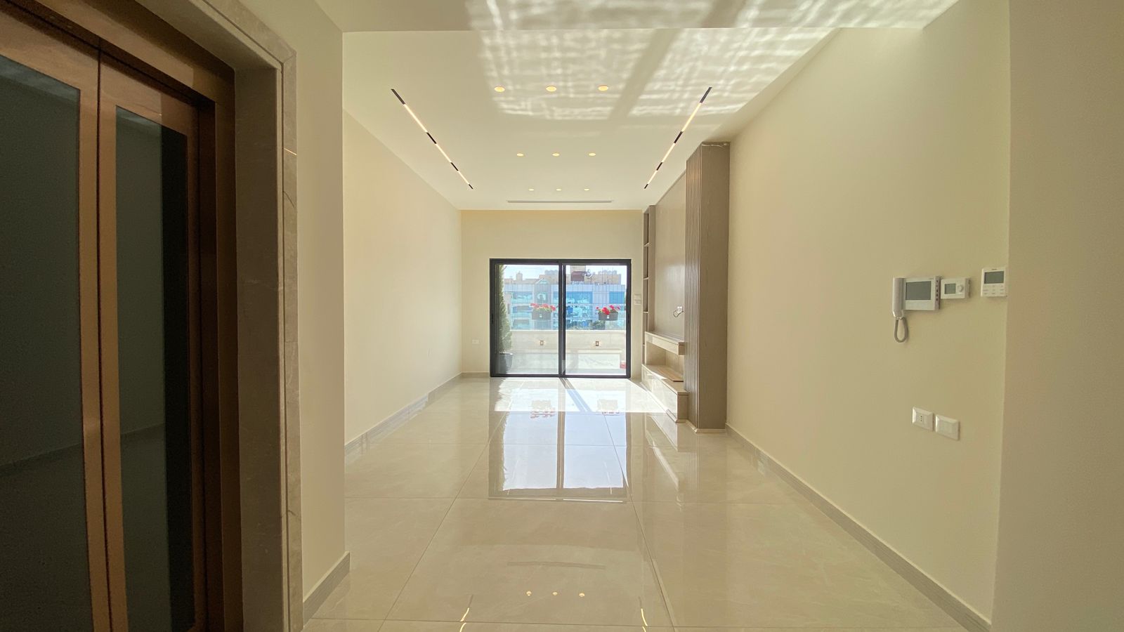 033edeb4-ee61-4ab6-af6c-98907c0629ef Empty modern hallway with a glossy tiled floor, sliding glass balcony door at the end, and built-in shelves on the right.
