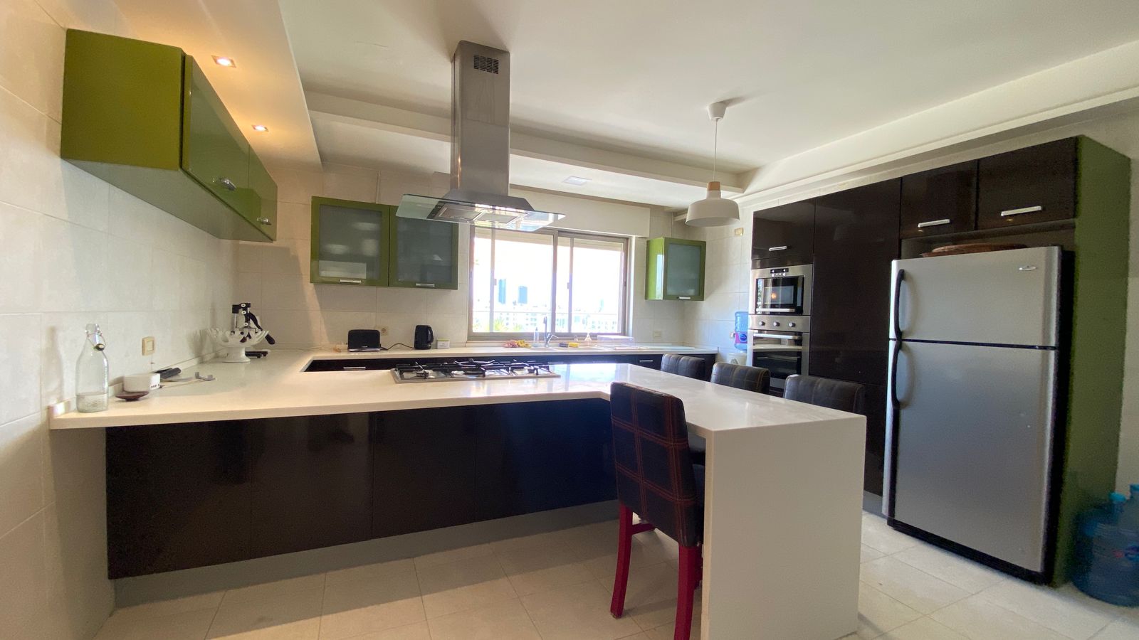 0369363d-e663-43b9-b891-bd0f74170772 Modern kitchen with black base cabinets, green wall cabinets, and a white island featuring a gas cooktop and stainless range hood in the center.