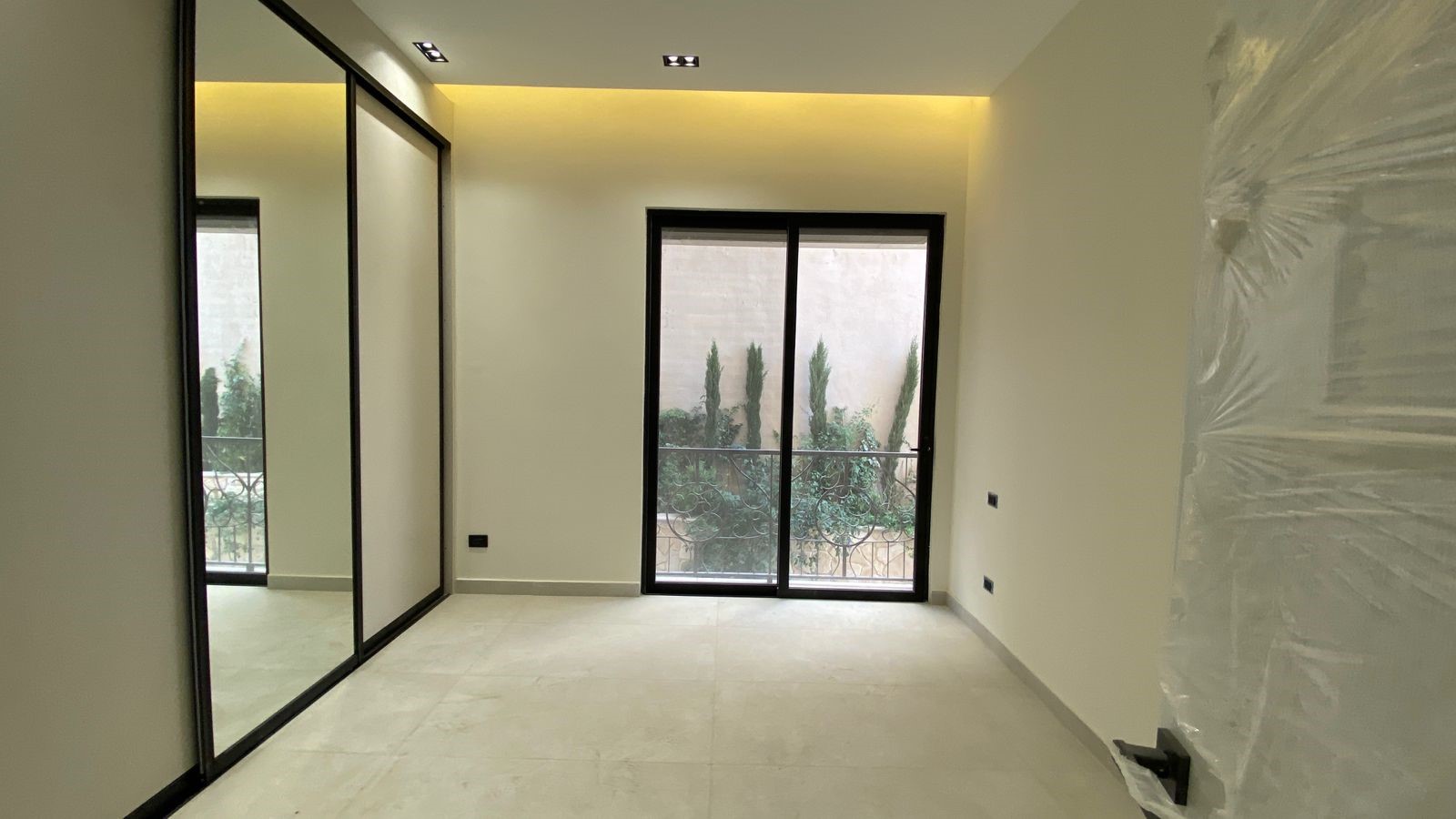 03be3daa-9561-4c72-a089-b3bb5f55270b Empty modern room with sliding mirrored wardrobes on the left and a glass balcony door showing trees outside