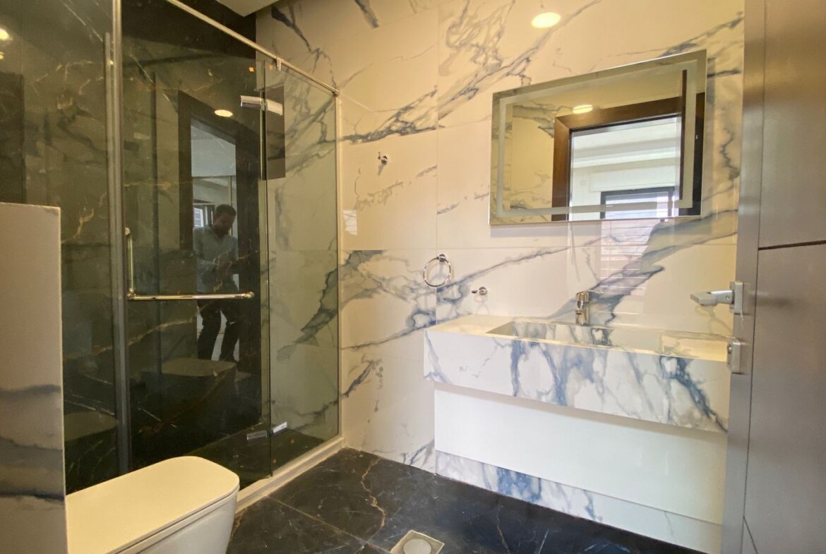 Marble bathroom with a glass shower enclosure, white-and-gray veined walls, and a marble countertop sink.