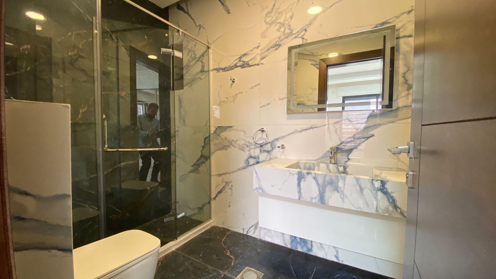 080d5b38-f941-4318-81f1-ec16164cbc52 Marble bathroom with a glass shower enclosure, white-and-gray veined walls, and a marble countertop sink.