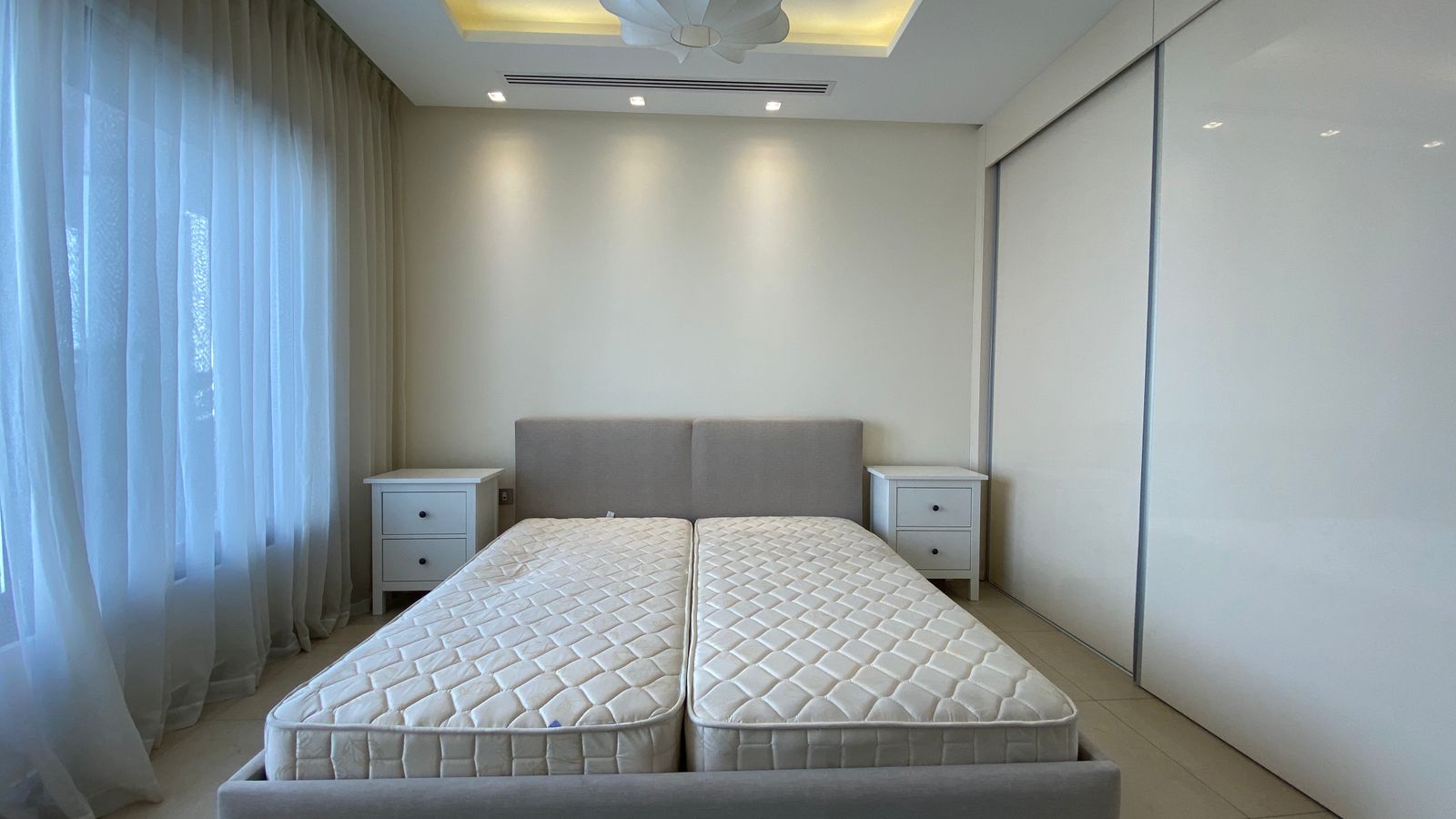 0a2ae03b-c263-4430-acf3-d07326469334 Minimalist bedroom with two adjacent twin mattresses on a low gray bed frame, flanked by white nightstands.