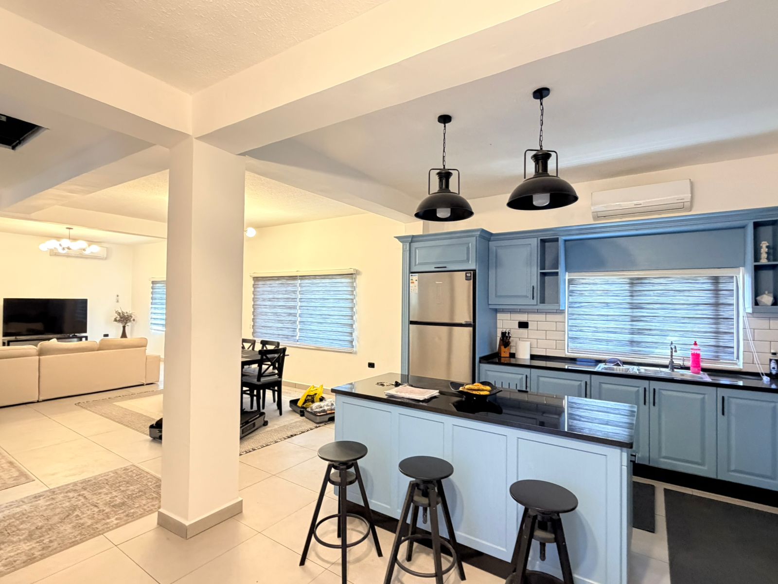 0b235fa2-8bd2-48eb-a4ea-438f0b6ed3de Open-plan kitchen with blue cabinets and black countertop island, stainless fridge, and four black bar stools.