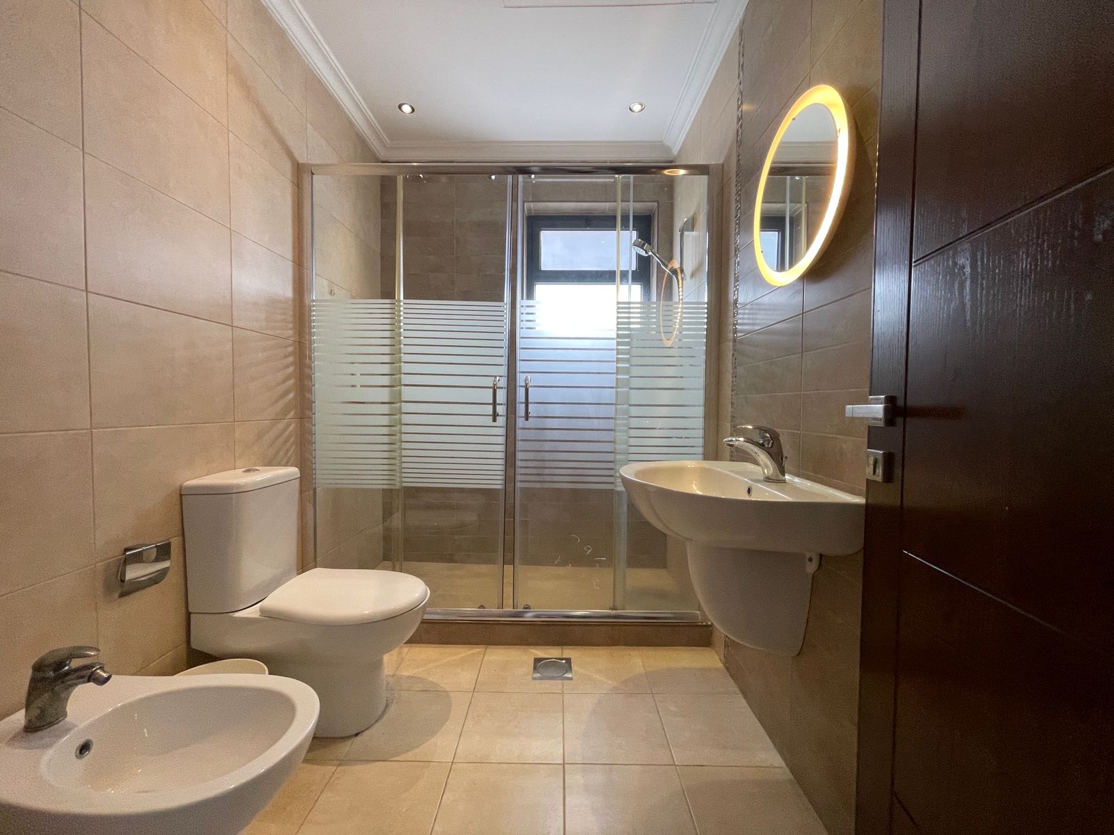 1049314e-cc4c-4fc9-b437-af358e2adbfc Modern bathroom with toilet, bidet, wall-mounted sink, and glass shower enclosure with frosted stripes.