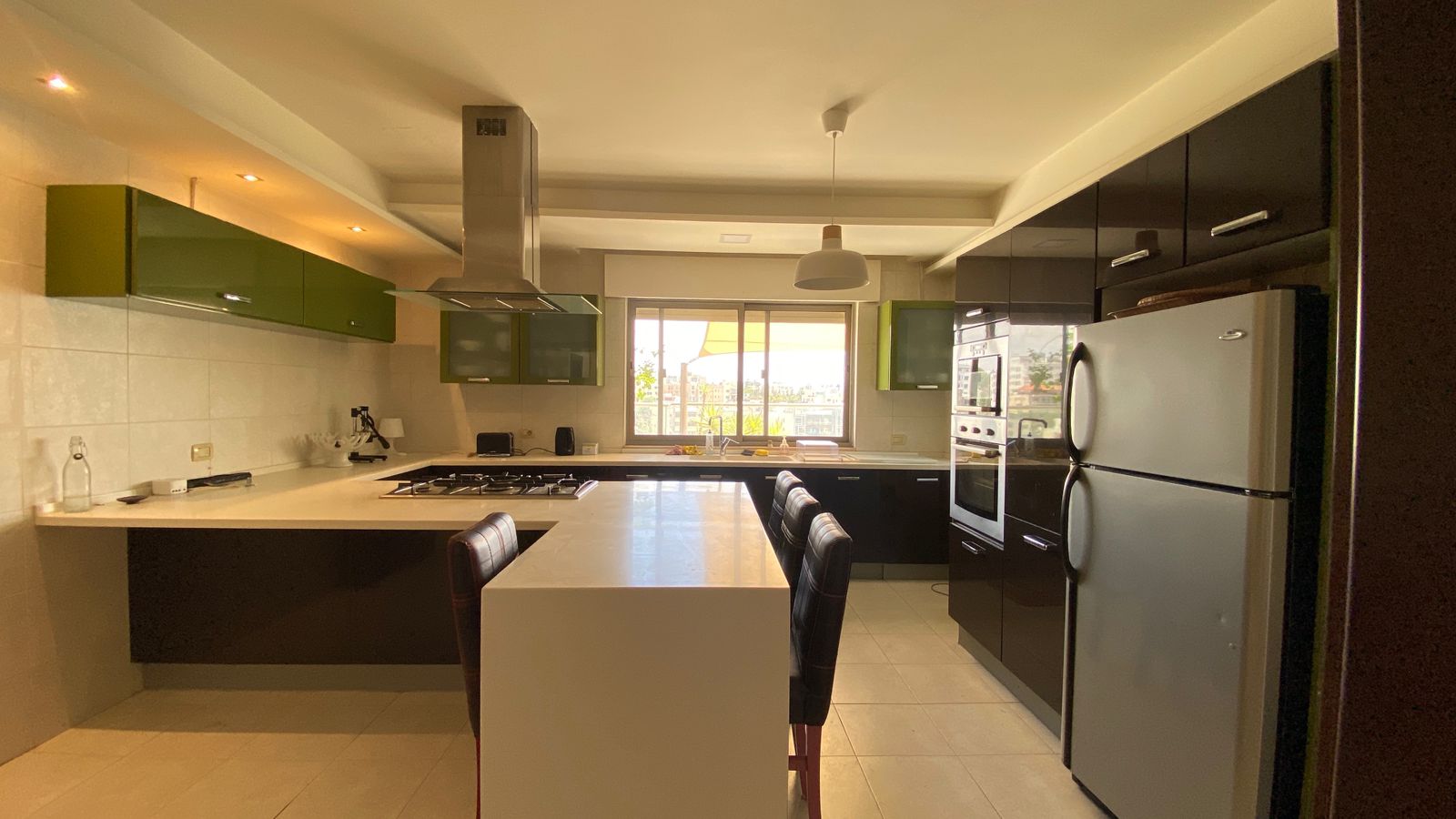 1901da27-008b-4384-b620-3fb760f1722b Modern kitchen with green upper cabinets, black lower cabinets, stainless steel appliances, and a central island with a gas cooktop.