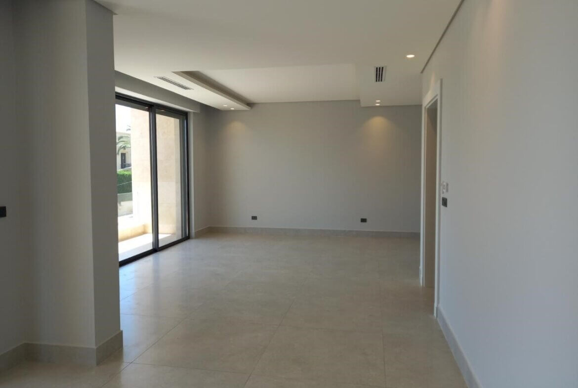19fbc04b-d69f-4460-8f22-52c8e983cdba Empty modern living room with beige tiled floor, light gray walls, and large sliding glass doors to a patio/outdoor space at left edge of the room.