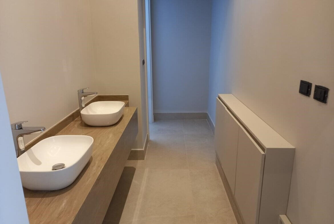 1a2c92d2-de71-49c4-bb29-edae1b9b82ee Modern bathroom with two white vessel sinks on a wooden countertop and a long wall cabinet to the right.