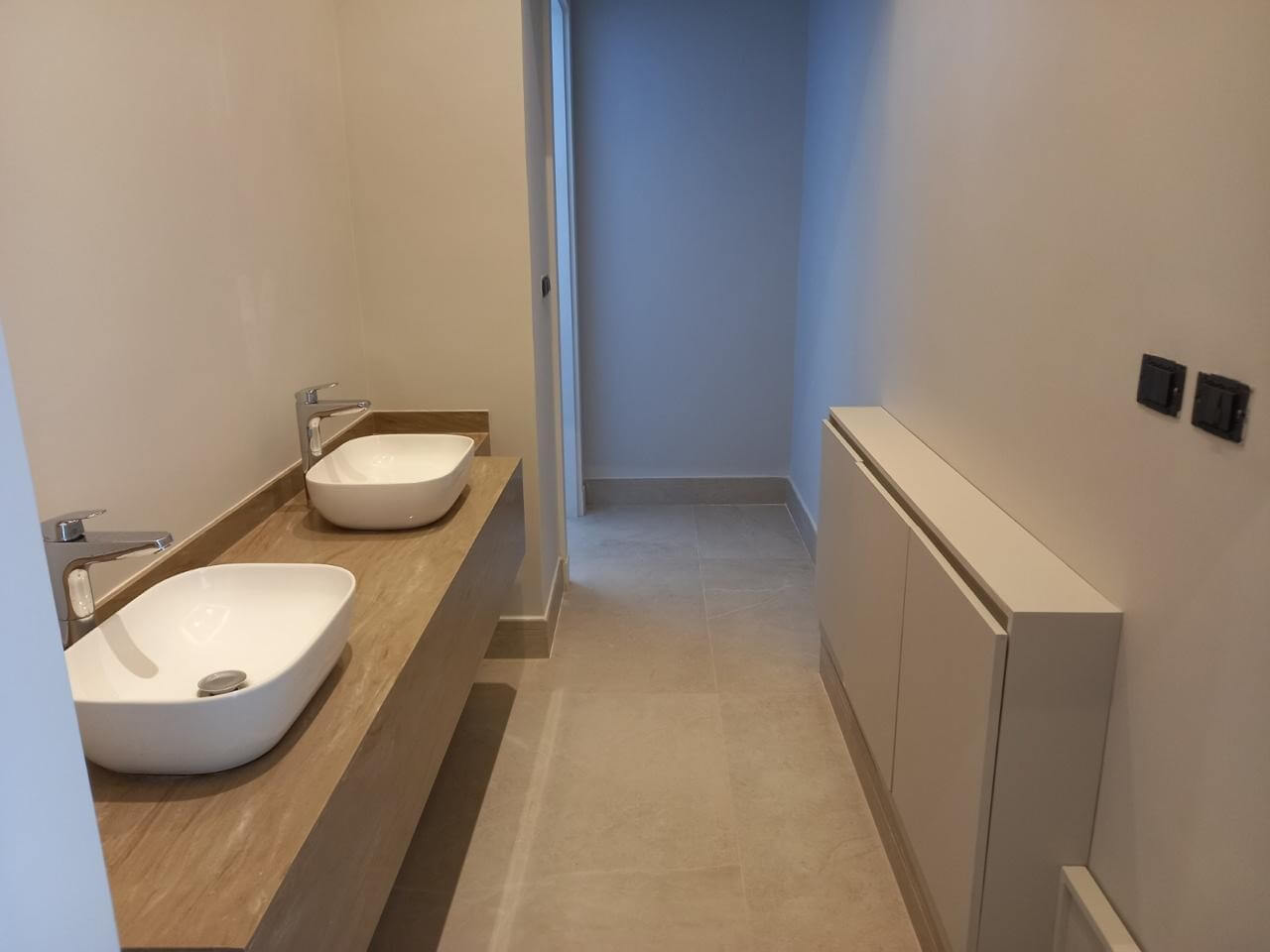 1a2c92d2-de71-49c4-bb29-edae1b9b82ee Modern bathroom with two white vessel sinks on a wooden countertop and a long wall cabinet to the right.