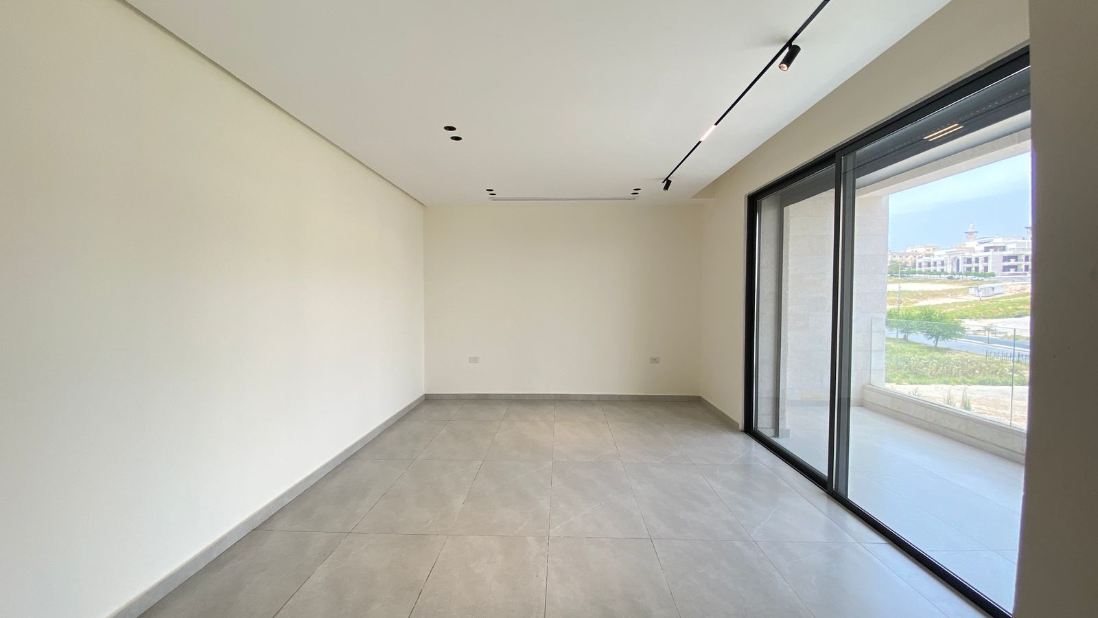 1c4a49c6-96a8-46e3-8a15-6f56323a2fde Empty modern living room with sliding glass doors to a balcony and grey floor tiles.지(Note: remove)