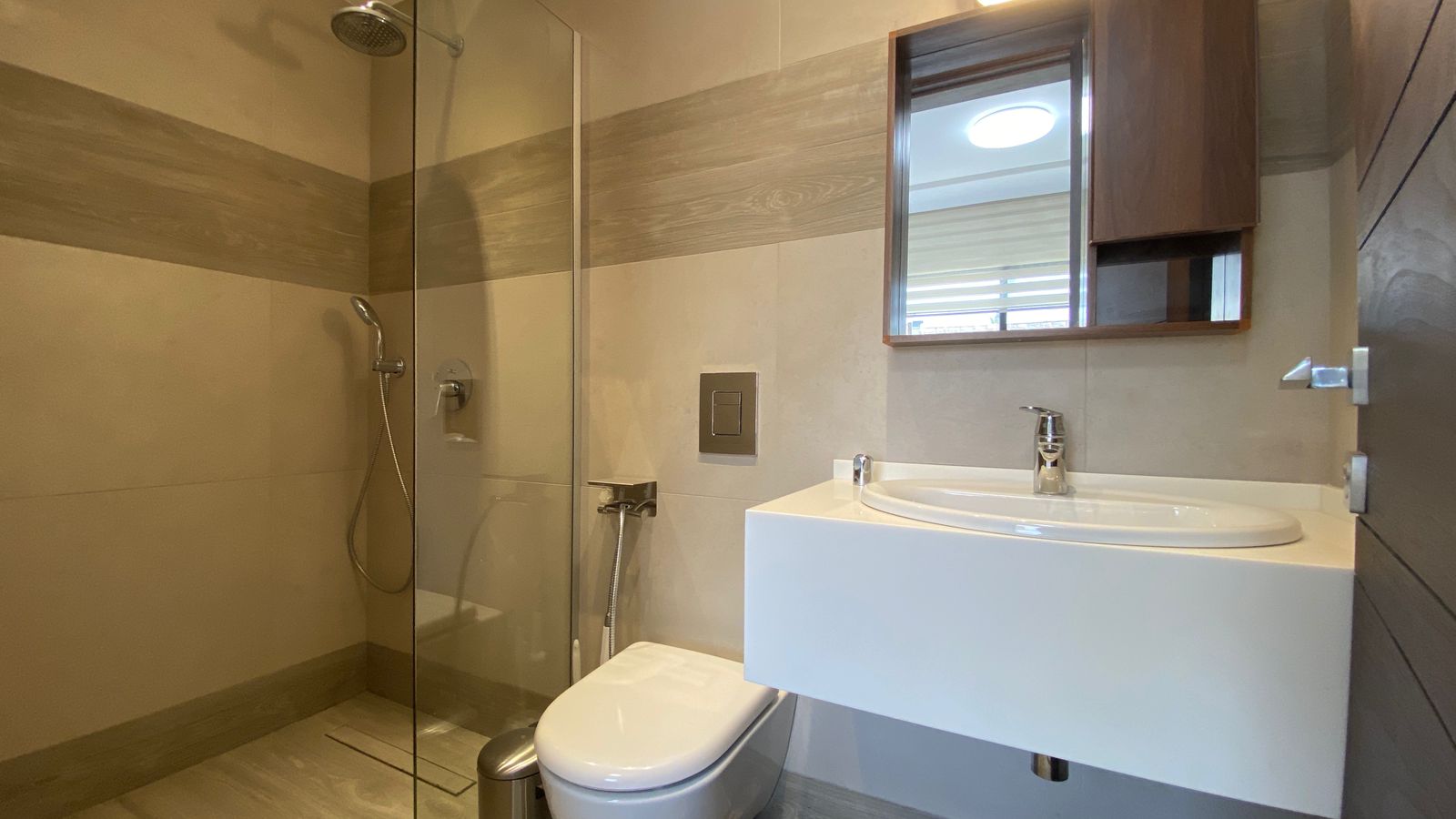 1d50d87d-14f4-4a6b-a9af-cdb1e6aadf8d Contemporary bathroom with glass-walled shower, wall-mounted toilet, and white sink with chrome faucet under a wooden mirrored cabinet