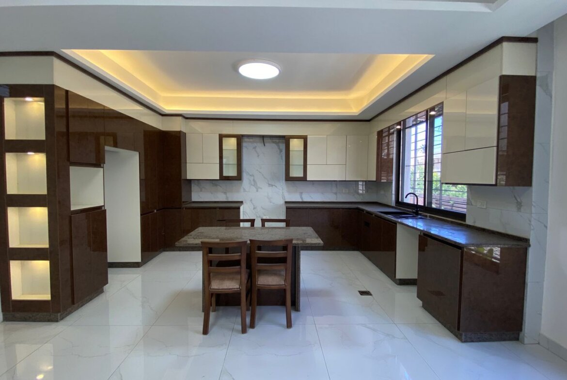 Modern L-shaped kitchen with brown and cream cabinets, marble backsplash, and a central dining table with four chairs.