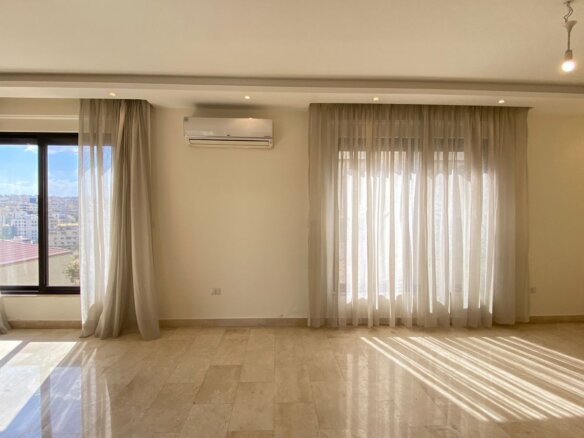 Bright, empty living room with large windows, sheer white curtains, and sunlight reflections on a marble floor.