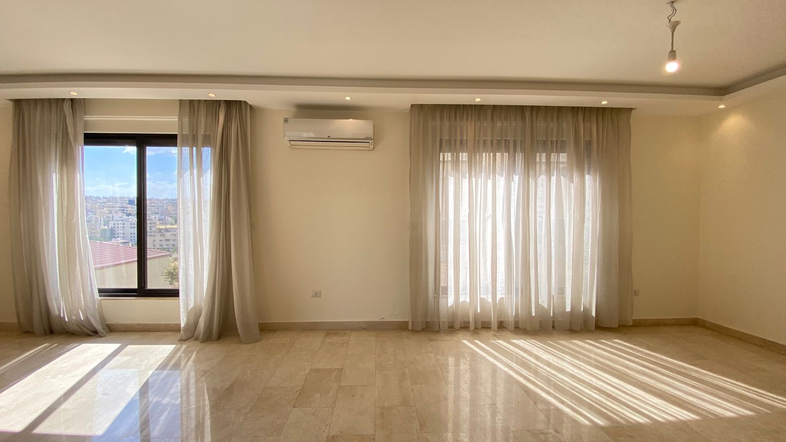 24ed70e5-ec10-436a-b081-b31878907b89 Bright, empty living room with large windows, sheer white curtains, and sunlight reflections on a marble floor.