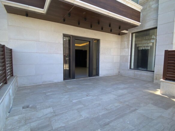 Outdoor tiled patio with beige stone walls, brown privacy fencing, and double glass doors opening to an interior space.