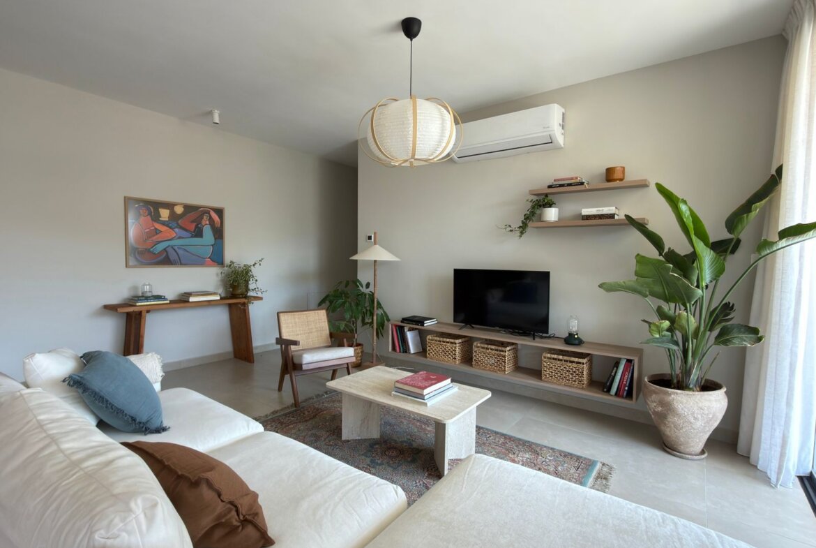 Bright living room with white sectional sofa, blue and brown pillows, and a low coffee table on a patterned rug.