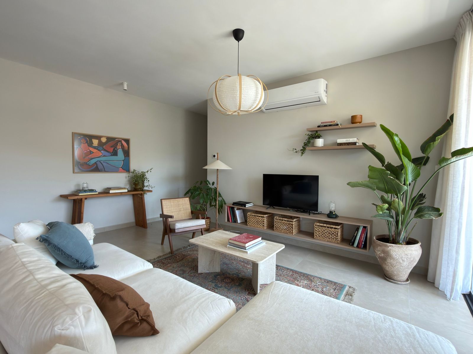 27c8e182-0b92-4213-9d63-809a56e86441 Bright living room with white sectional sofa, blue and brown pillows, and a low coffee table on a patterned rug.