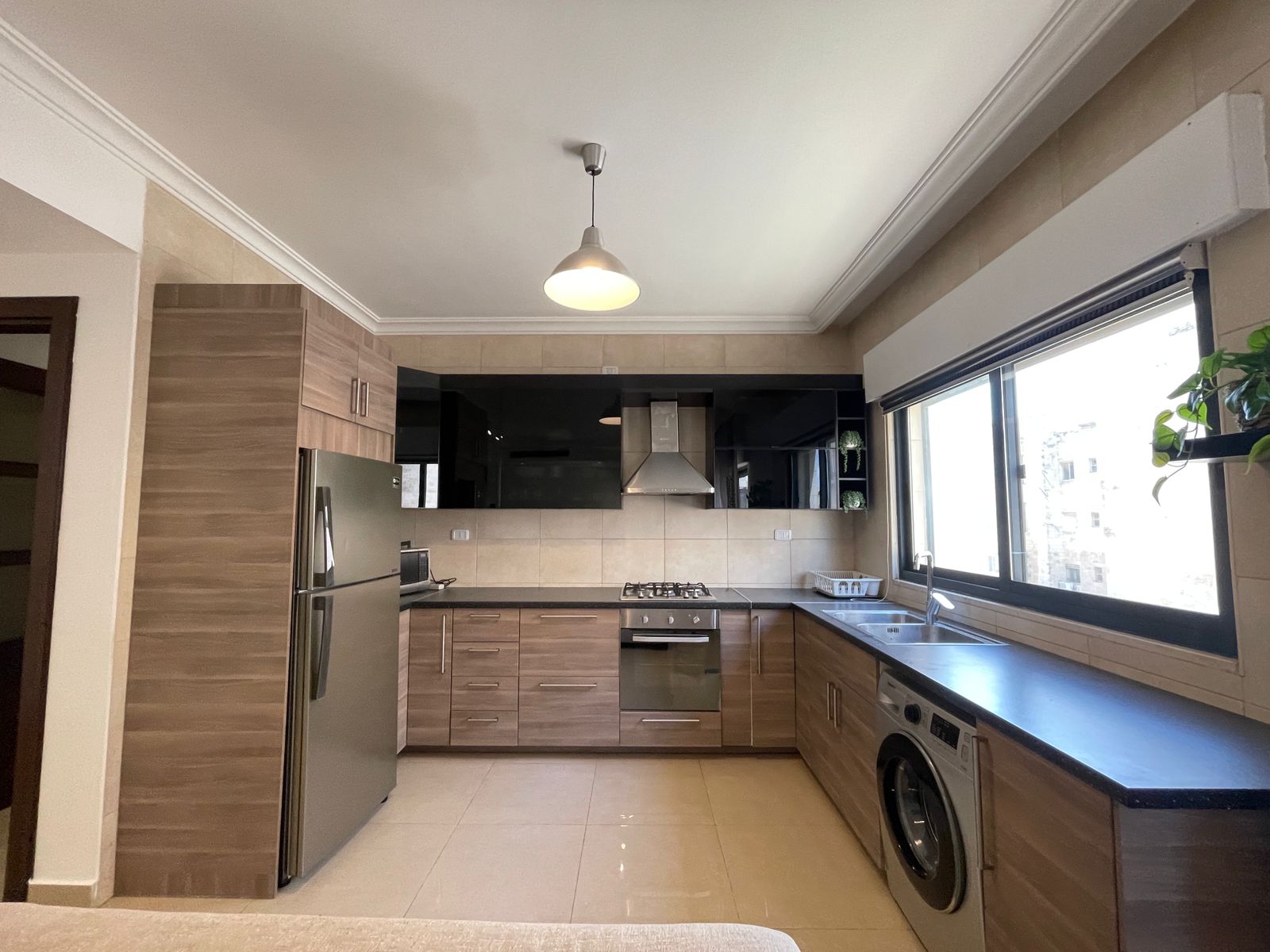 2947a0e7-a72b-41e5-9b5f-d6eb0f7860fc Modern L-shaped kitchen with wood veneer cabinets, stainless fridge, gas range and chimney hood under a row of black upper cabinets