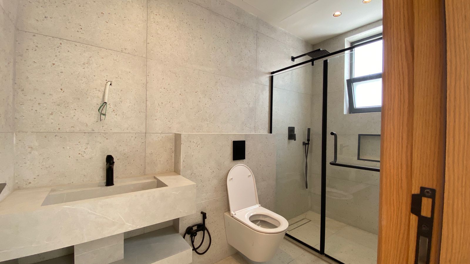 2d41f346-01a6-4f3e-819d-b66246151441 Modern bathroom with a marble vanity, wall-mounted faucet, and wall-hung toilet beside a glass shower enclosure.
