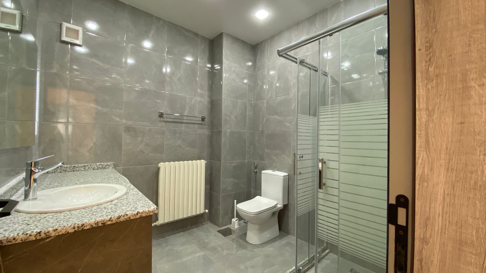 327631aa-ad0d-4950-beae-88ccb015f8c7 Modern gray tiled bathroom with granite vanity, oval sink, chrome faucet, and mirror (bathroom fixtures visible).