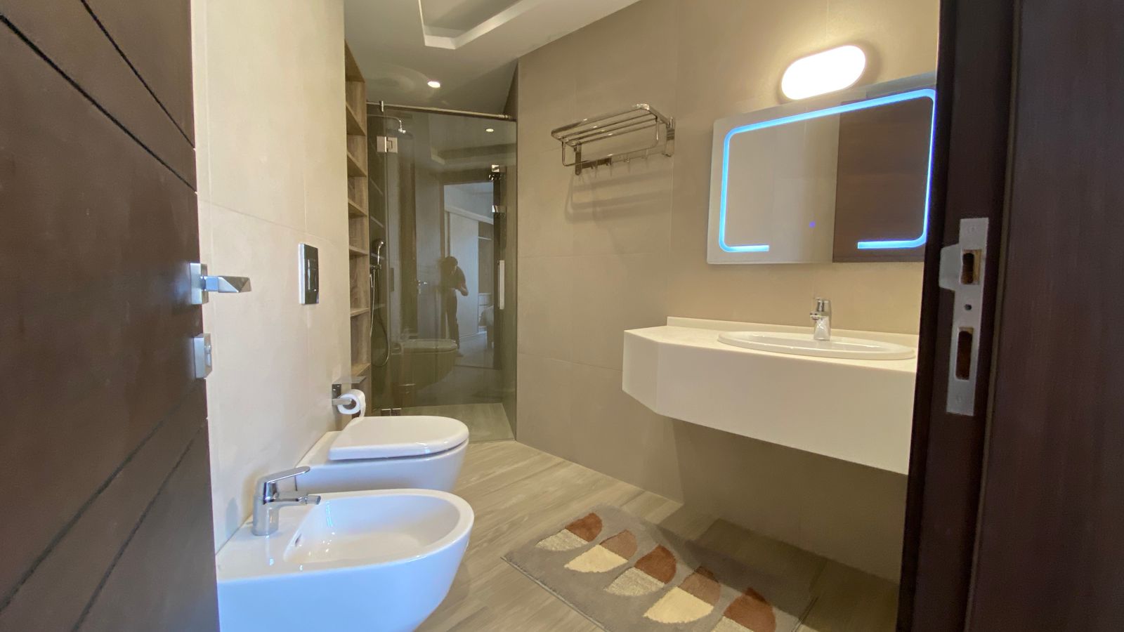 35f7ba38-a5f4-4809-a788-ab587b545e64 Modern bathroom with glass shower, wall-mounted sink with a backlit mirror, toilet and bidet.