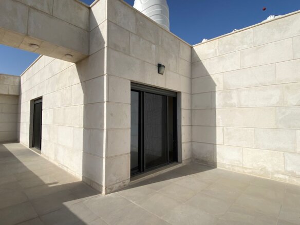 Beige stone courtyard with a sliding glass door and a shaded doorway on the left, under a clear blue sky.