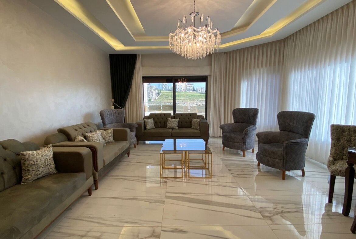 Luxurious living room with marble floor, grey sofas, chandelier, and large windows with sheer curtains.