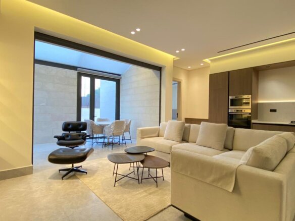 Bright open-plan living room with a cream sectional, black lounge chair with ottoman, and a set of round coffee tables near a glass patio door to an outdoor seating area.