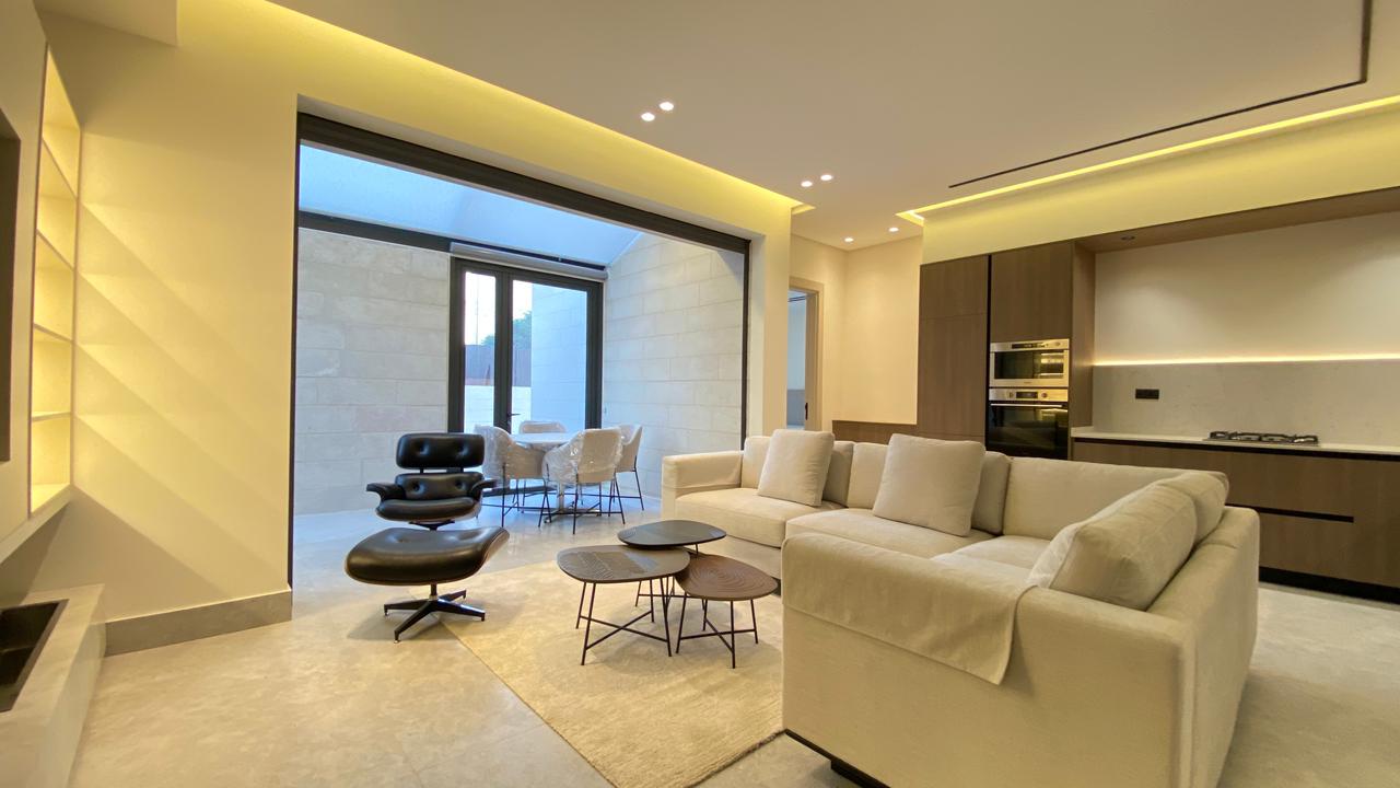 Bright open-plan living room with a cream sectional, black lounge chair with ottoman, and a set of round coffee tables near a glass patio door to an outdoor seating area.