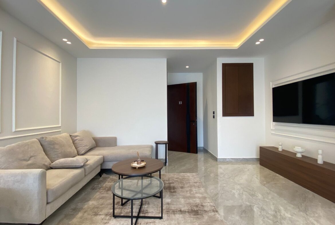 Modern living room with a light beige sectional sofa, round coffee tables, and a textured rug under a TV wall and low wood console.