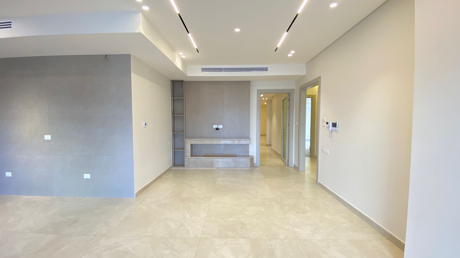 3c6ced33-b8eb-4871-9d4d-74c592c62012 Empty modern living area with a gray tile feature wall on the left, built-in alcove/storage unit, and a hallway at the back.