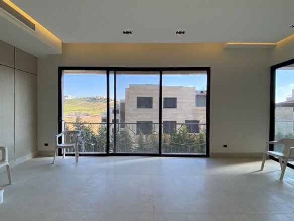Bright, unfurnished room with large sliding glass doors opening to a balcony; three white plastic chairs and a bucket on the pale floor.