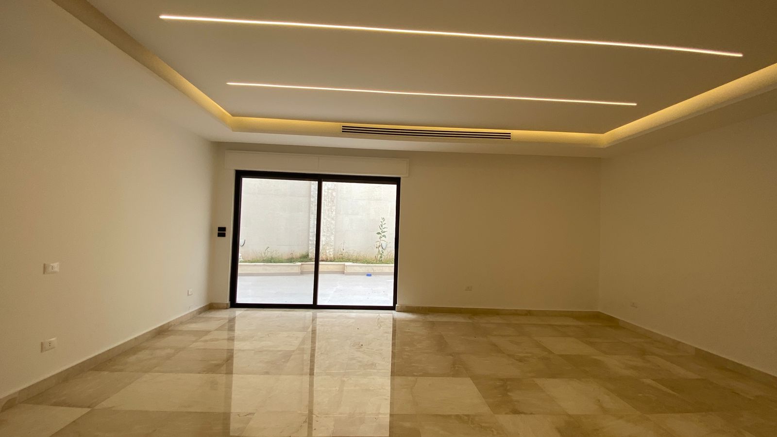 3d0925bd-105b-48ad-8d36-2bf57d63e98c Empty modern living room with marble tile floor and a large sliding glass door opening to an outdoor space.