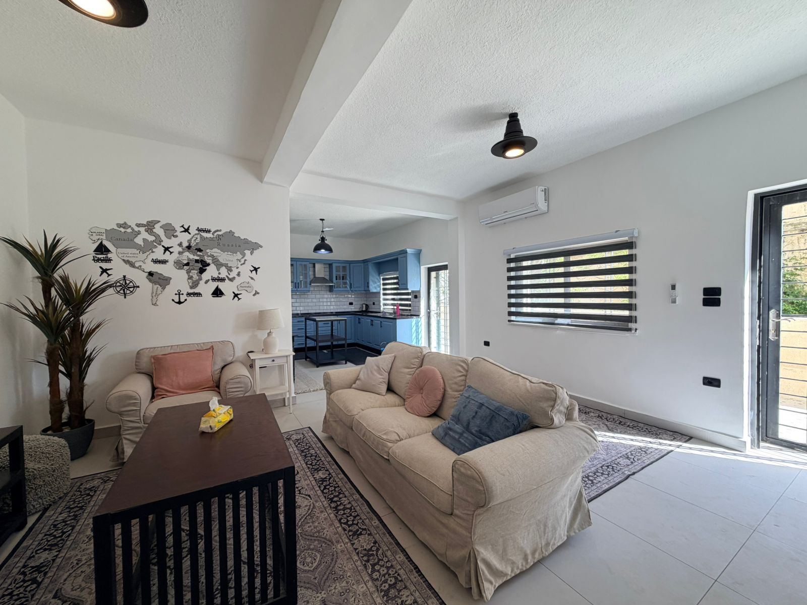 3f900479-4602-4487-9726-aed8af8a375f Living room with beige sofa, coffee table, and a wall map decal, open to the blue kitchen.