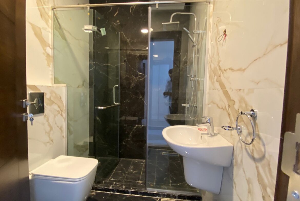 Modern bathroom with a glass-enclosed shower, white toilet, and wall-mounted sink set against marble walls.