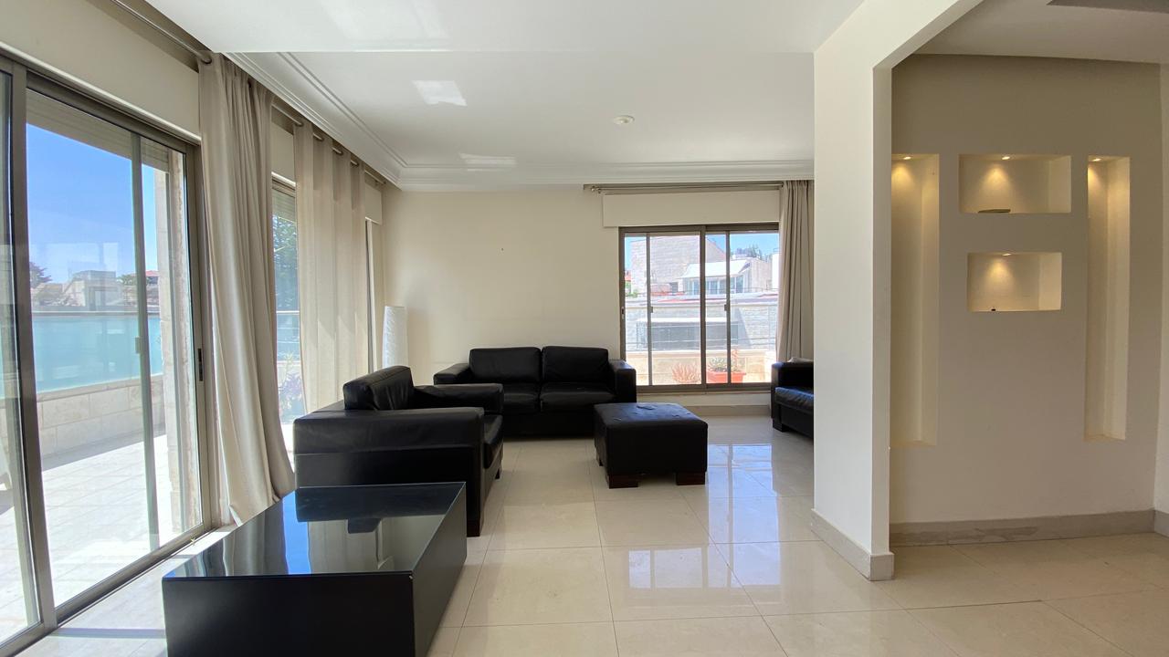 4057c622-720f-4dba-b1d1-a9126c769ff3 Bright living room with black leather sofas arranged around a glossy coffee table and large glass doors to a patio area, letting in natural light from outside, cream curtains in view.