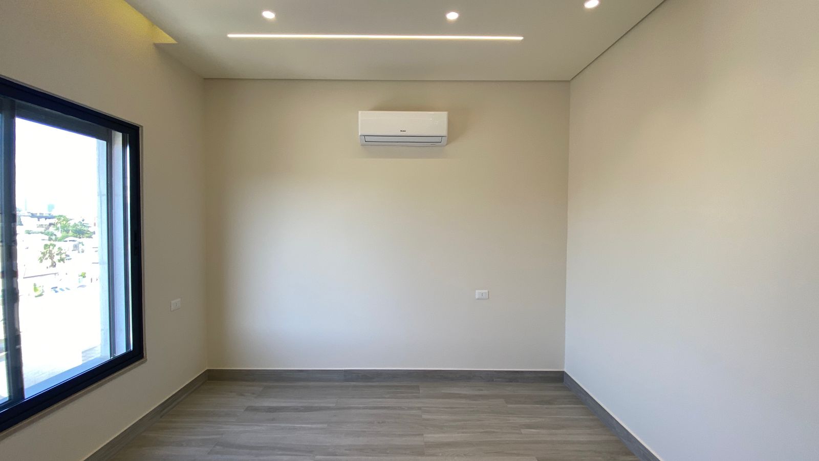 407f901c-3353-42f9-8c09-91d153f99292 Empty light-filled room with a wall-mounted air conditioner and a large window on the left.