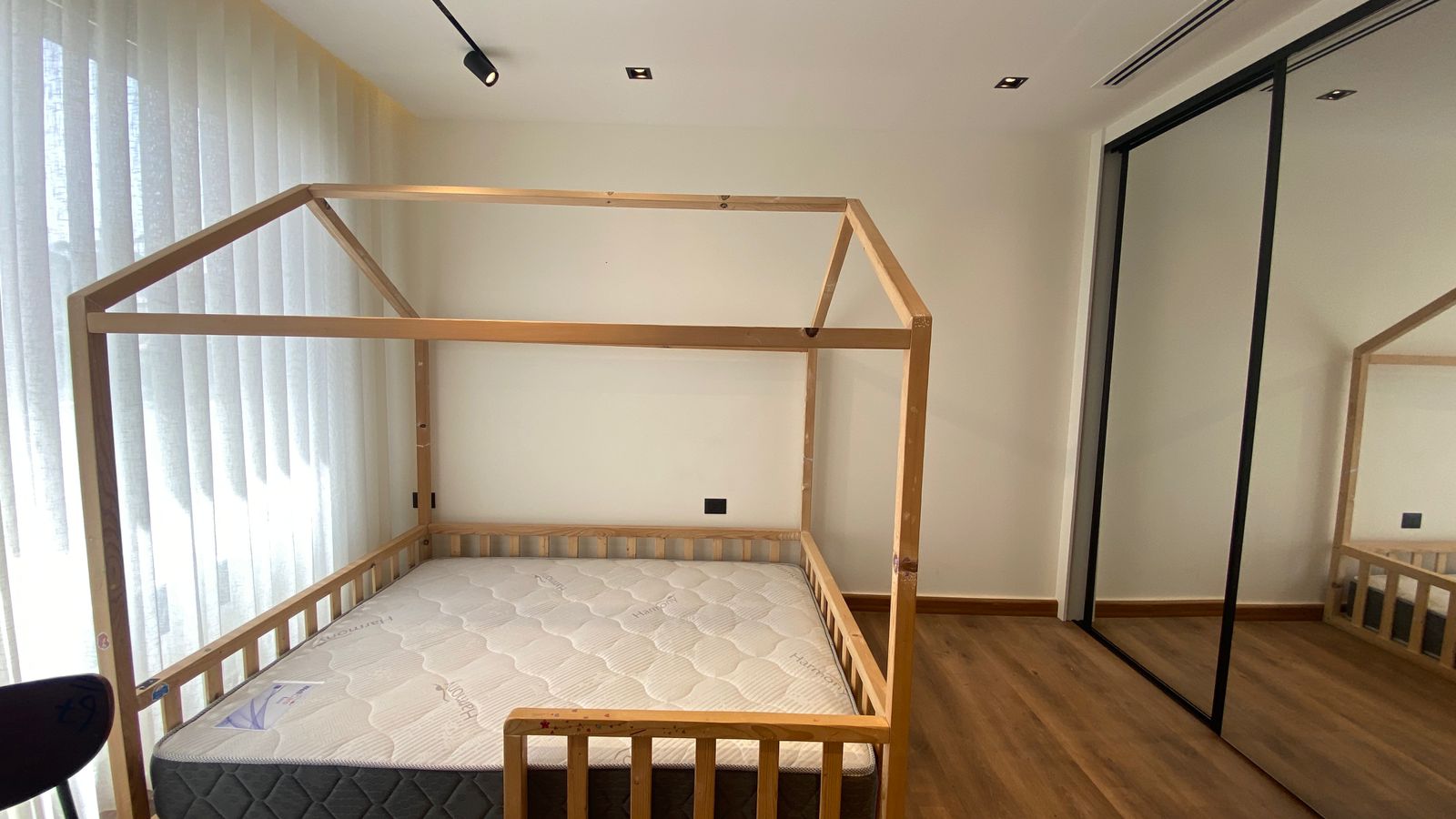 45c45663-b702-4110-9ca6-47139d036f54 Empty bedroom with a wooden house-frame bed and mattress, hardwood floor, and large mirrored wardrobe doors on the right.