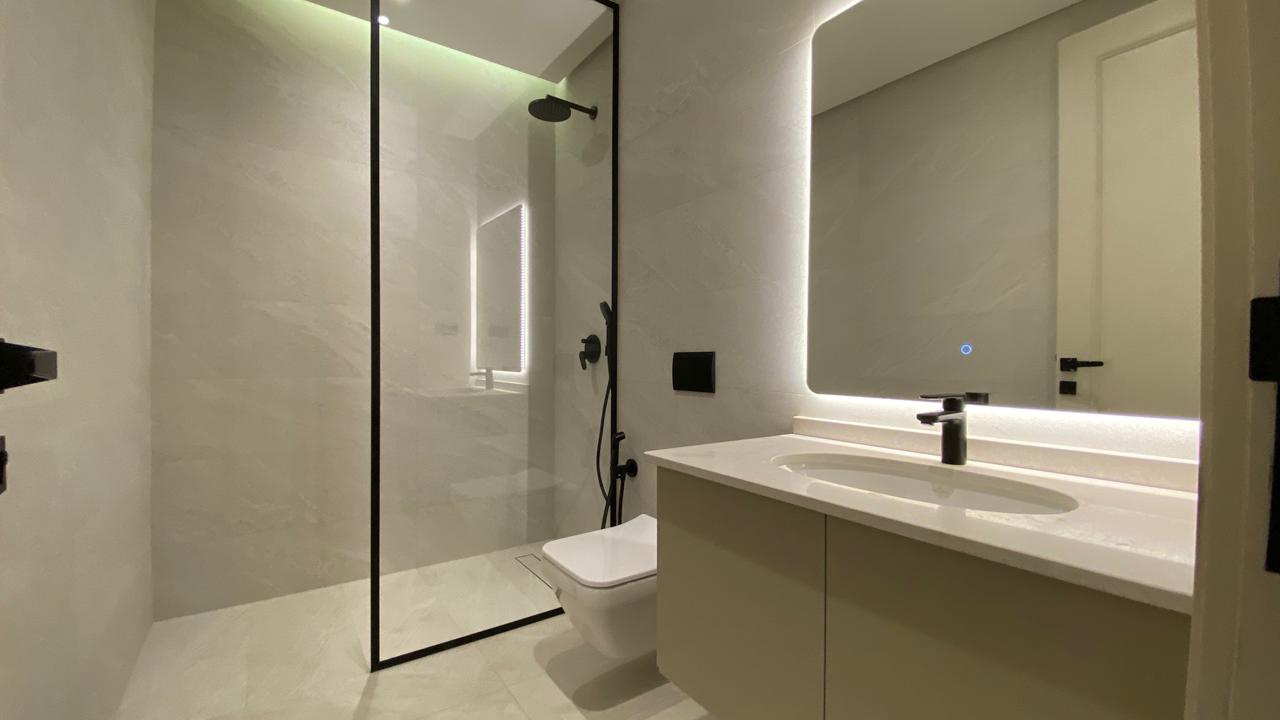 Modern bathroom with a glass-enclosed shower, white vanity, and backlit mirror in a minimalist gray space.