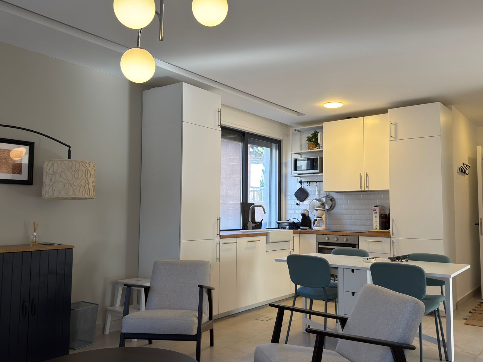 477d77ff-6250-4334-8f42-cbf9bc39a6f5 Open-plan kitchen with white cabinets, wooden countertops, stainless-steel appliances, and a dining table with blue chairs.