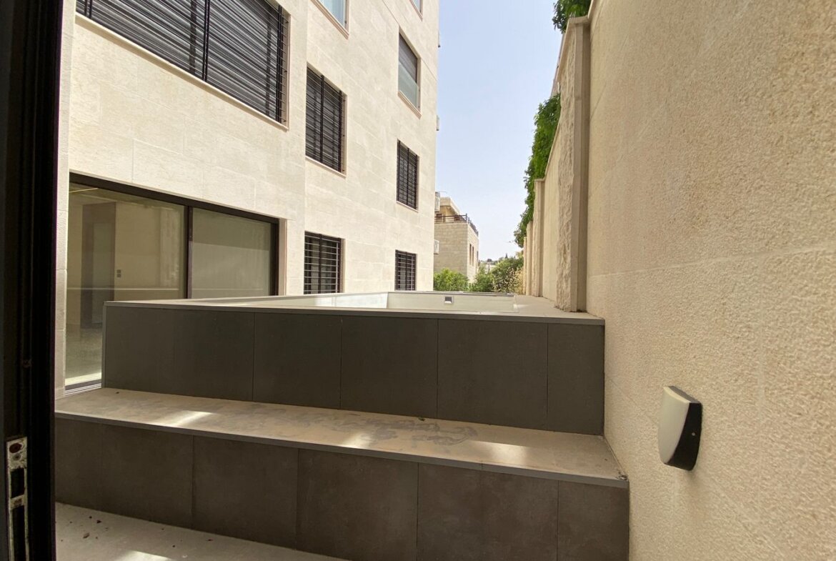 Outdoor courtyard between light stone buildings, featuring a dark gray raised platform and steps.