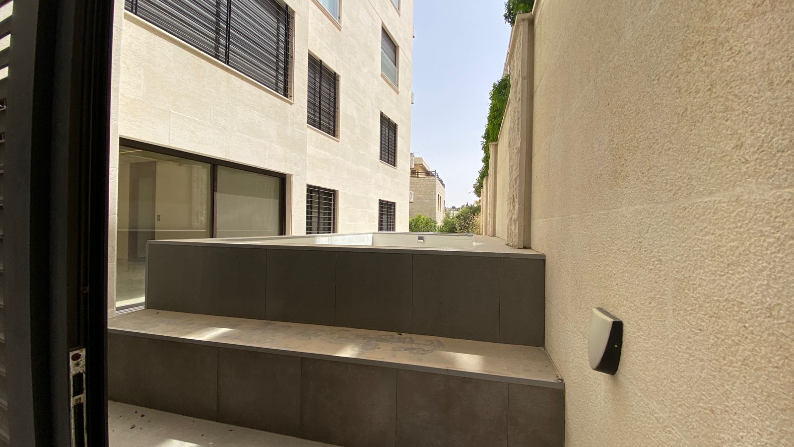 4816ca84-a4f4-4ddc-97d5-78c0d180ef50 Outdoor courtyard between light stone buildings, featuring a dark gray raised platform and steps.