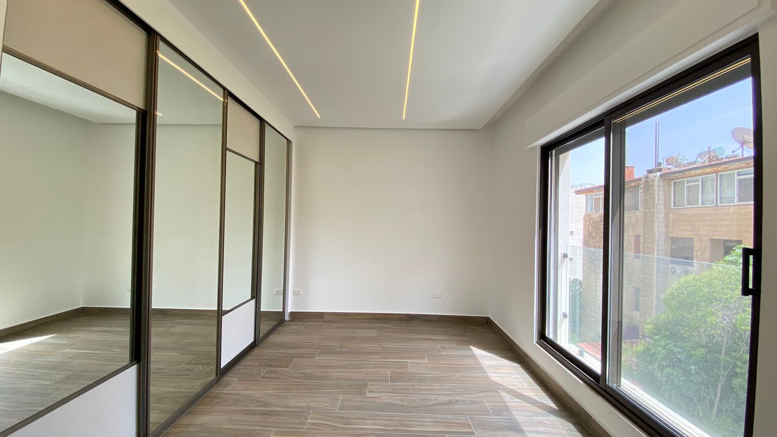 48638d10-80f7-4585-925b-61d5738c3462 Bright empty room with wide windows on the right, a glass-partition wall on the left, and a wood-look tile floor.