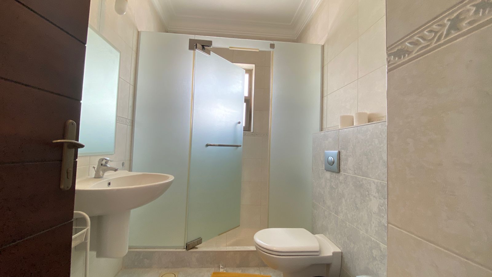 499c9dfd-f161-4a8f-83c5-d479a338dfc3 A small bathroom with frosted glass shower doors, a pedestal sink, and a wall-mounted toilet.