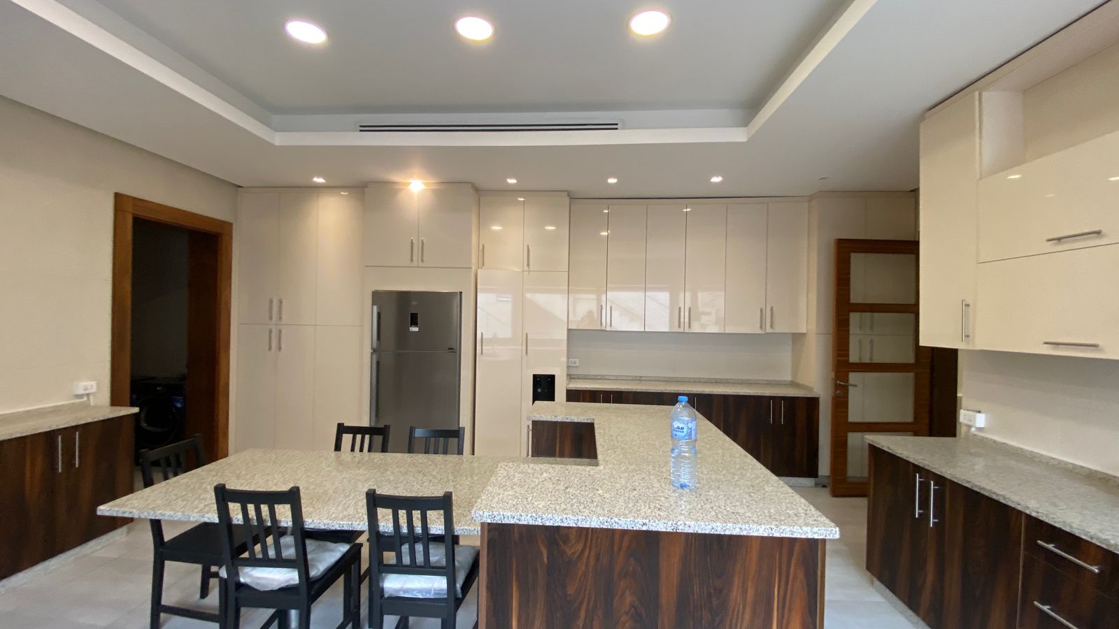 4cb23302-49fd-4ca3-92b1-8c1562340342 Contemporary kitchen with white upper cabinets, dark wood lower cabinets, and a large granite island.